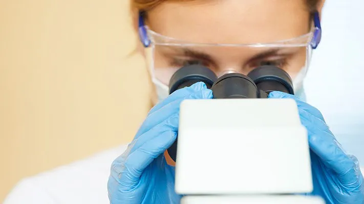 Pathologist examining a biopsy sample under a microscope to diagnose stage 2 stomach cancer