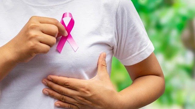 Person wearing a white shirt holding a pink ribbon on the chest to raise awareness for breast cancer prevention