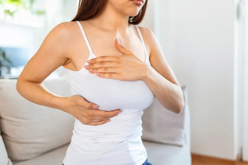 Woman performing a breast self-exam to check for pain or abnormal symptoms that may indicate breast cancer