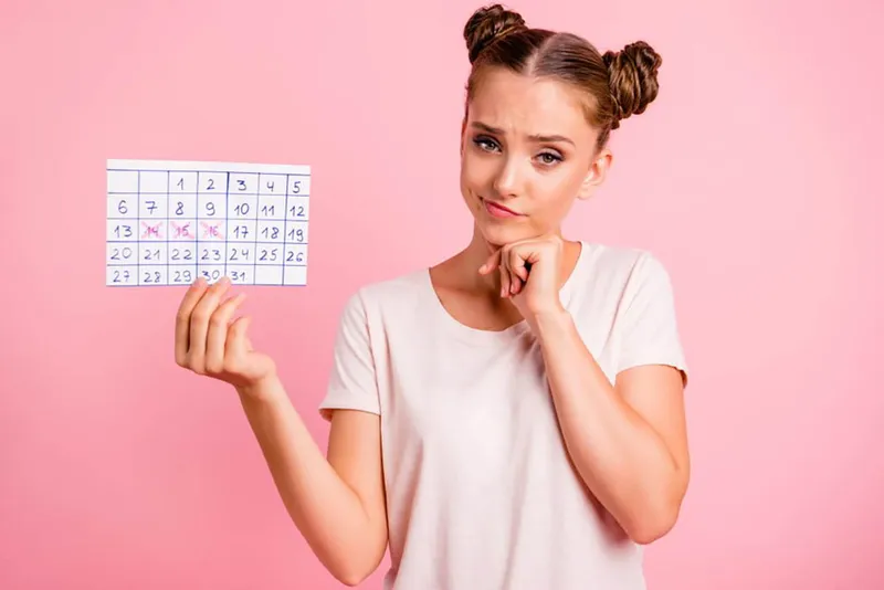 Young woman holding a menstrual calendar looking concerned about irregular periods, which can increase breast cancer risk