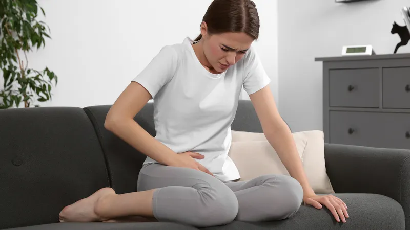 Woman sitting on a couch holding her lower abdomen in pain, illustrating the silent progression of cervical cancer symptoms