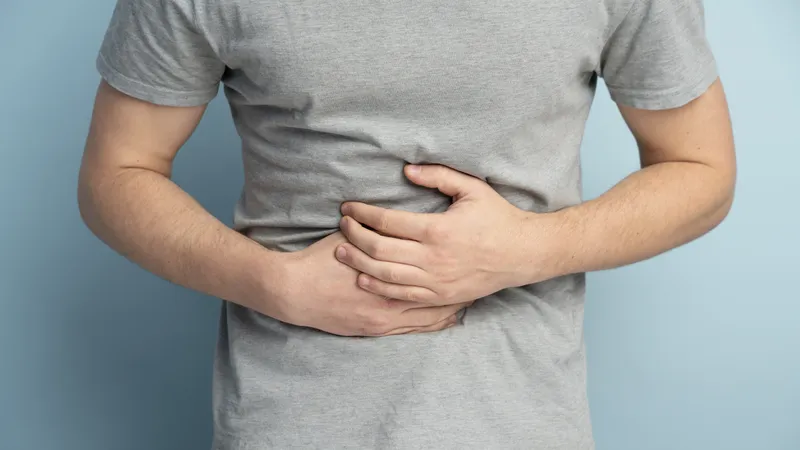 Person holding stomach with upper abdominal pain, a possible symptom of stomach cancer
