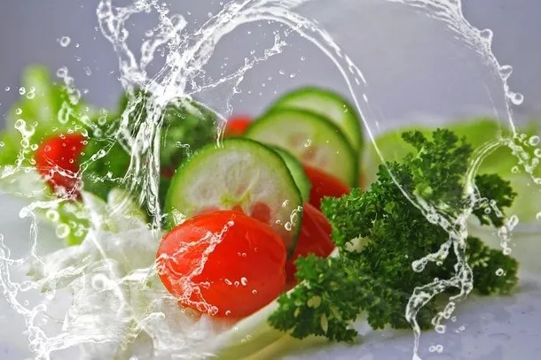 Fresh cucumbers, tomatoes, and parsley splashed with water, representing hydrating fruits and vegetables for healthy skin
