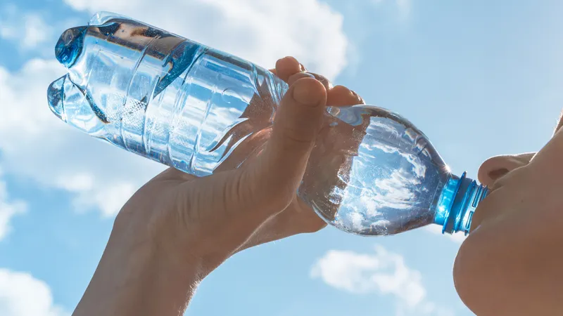 A person drinking water from a plastic bottle under the blue sky to stay hydrated and prevent dry eyes.