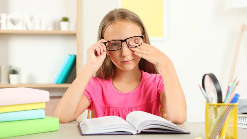 A young girl covering one eye while reading, showing symptoms of eye redness due to allergies.