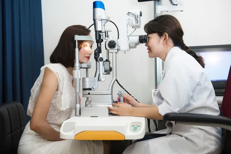 A patient undergoing an eye examination with a slit lamp performed by an ophthalmologist at an eye clinic.