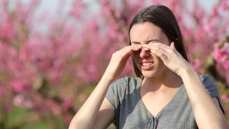 A woman rubbing her itchy eyes outdoors during allergy season