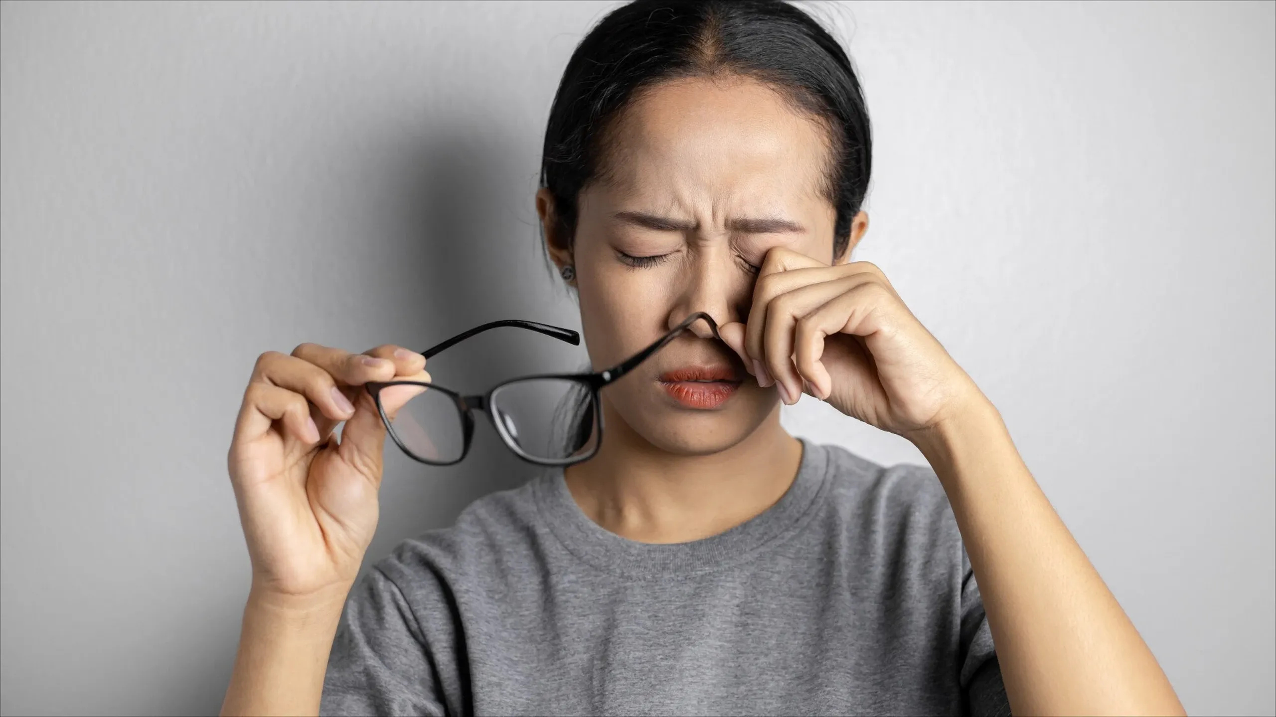 A woman rubbing her eyes while holding her glasses, showing signs of visual discomfort and possible vision impairment.