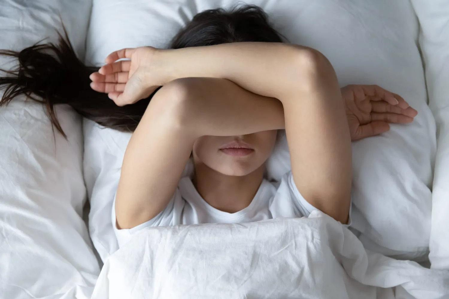 Woman lying in bed covering eyes due to pain interfering with sleep
