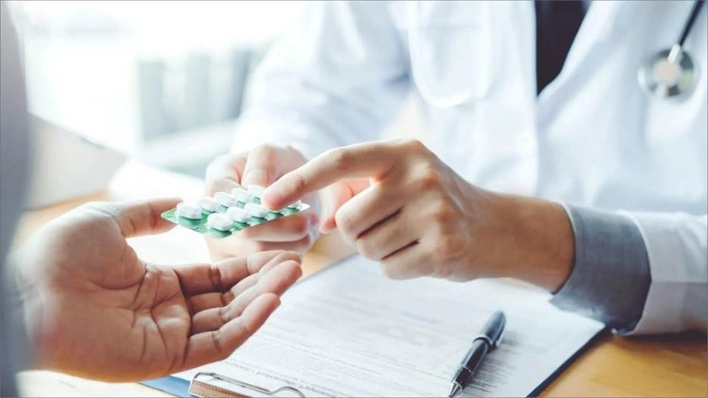 A doctor handing a blister pack of pills to a patient during a consultation for atrophic tonsillitis treatment