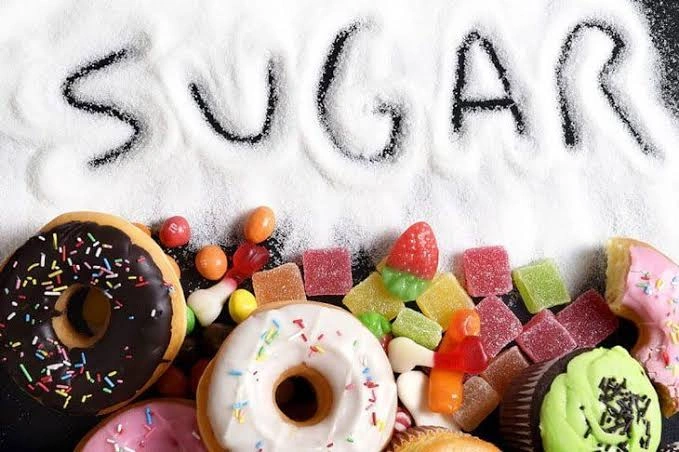 Assorted sugary sweets, donuts, and candies surrounding the word SUGAR written in white sugar powder, illustrating high sugar consumption and dental risks