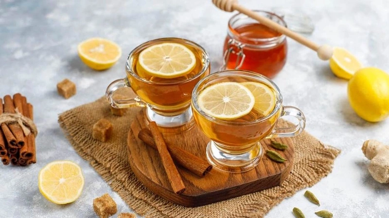 Two glass cups of warm lemon tea with honey, cinnamon sticks, and ginger slices on a table for soothing tonsillitis symptoms