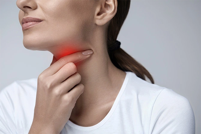 A woman in a white t-shirt pointing to her throat, marked with a red glow, indicating a progressive sore throat as a typical symptom of atrophic tonsillitis