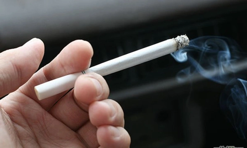 Voice Disorders A hand holding a lit, smoking cigarette in a dark environment, representing smoking as a significant risk factor for developing voice disorders