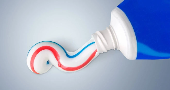 A close-up view of a blue toothpaste tube squeezing out striped red, white, and blue fluoride toothpaste
